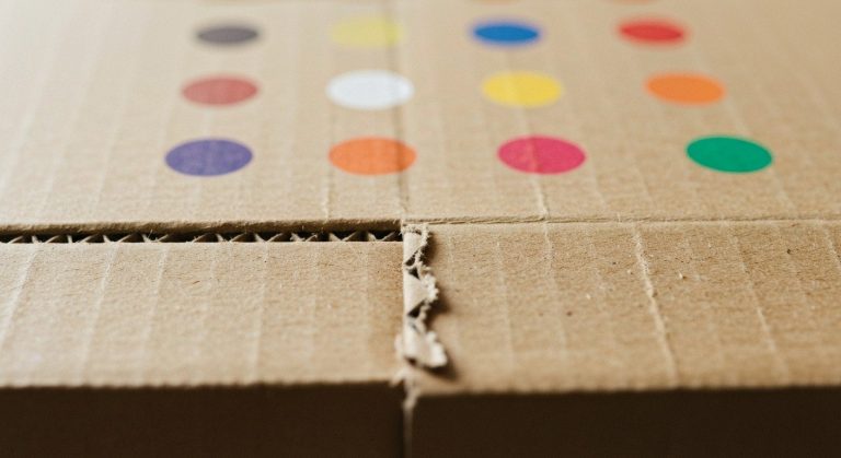 Close-up of small blue, red, yellow, and black circles printed on the edge of a brown cardboard box flap.