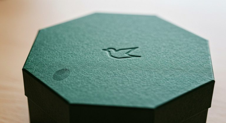 A forest green octagonal gift box with a bird emblem sits on a limestone table in soft window light.