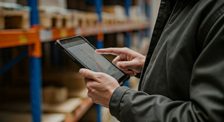 Warehouse worker using a tablet near organized inventory shelving, shallow depth of field focus.