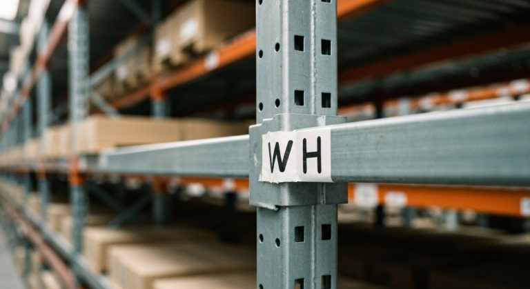 A close-up of a warehouse shelf label with the abbreviation WH on a metal rack.