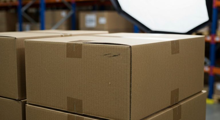 Stacks of plain cardboard boxes in a bright, modern warehouse setting, focus on texture and lighting.